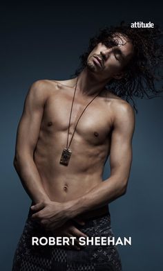 a shirtless man with long hair standing in front of a dark background and wearing a necklace