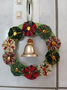 a christmas wreath hanging on the wall with a bell attached to it's side