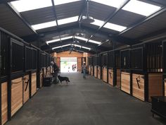 the inside of a horse barn with stalls and people walking through it on either side