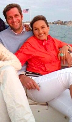 two men and a woman are sitting on a boat in the water, smiling at the camera