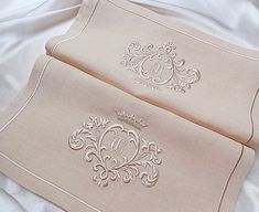 two white pillows on top of a bed covered in sheets and pillow cases with embroidered monograms