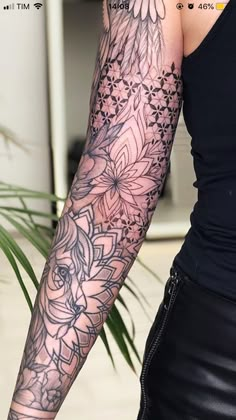 a woman's arm with flowers and leaves tattooed on her sleeve, in front of a potted plant