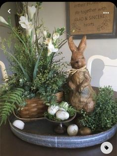 a bunny statue sitting on top of a table next to plants and eggs in bowls