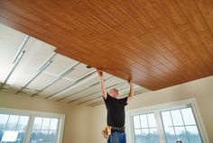 a man working on a ceiling in an empty room with windows and wood paneling