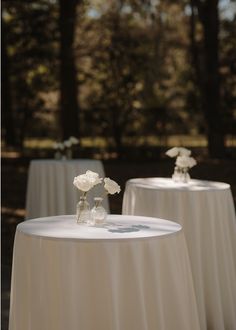 two tables with white flowers in vases sitting on top of each other near trees