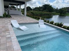 an empty swimming pool with two lounge chairs next to it and a lake in the background