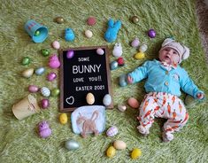 a baby laying on the ground next to an easter sign with some bunny eggs around it