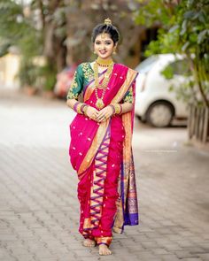 a woman in a pink and green sari is standing on the street with her arms crossed