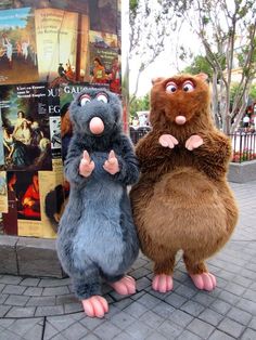 two stuffed animals standing next to each other on a brick walkway in front of a movie poster