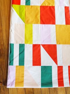 an orange, yellow and green patchwork quilt on a wooden floor next to a pair of scissors