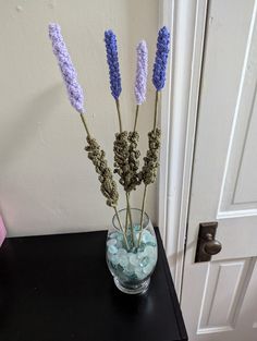 three lavender flowers in a glass vase on a black table next to a white door