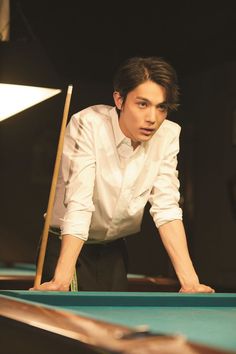 a man leaning over a pool table with a cue in his hand and looking at the camera