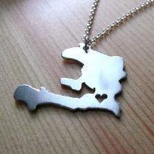 a silver necklace with a heart in the shape of a map on top of a wooden table