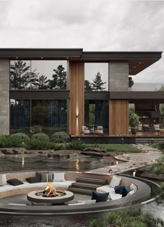 an outdoor fire pit in front of a modern house with water and trees around it