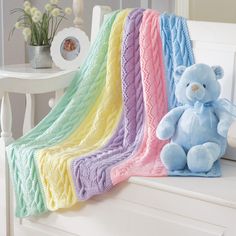 a blue teddy bear sitting on top of a white bed next to a rainbow blanket