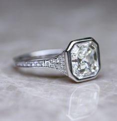 a diamond ring on a white surface with diamonds around it and the center stone is surrounded by small pave stones