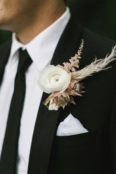 a man in a black suit with a white flower and feather boutonniere