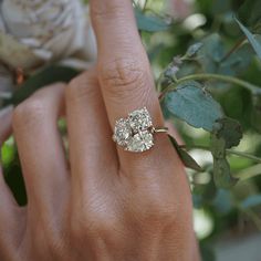 a close up of a person's hand with a ring on their finger and flowers in the background