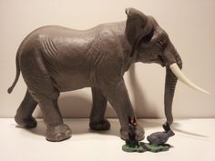 an elephant with tusks standing next to a small gray animal on a white surface