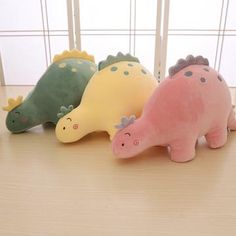 three stuffed dinosaurs are lined up on the floor