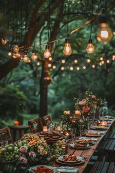 an outdoor dinner table is set up with lights and plates on it, surrounded by greenery