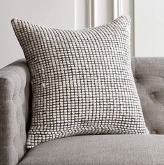 a black and white pillow sitting on top of a gray couch next to a window