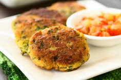 two crab cakes on a white plate next to a bowl of vegetables