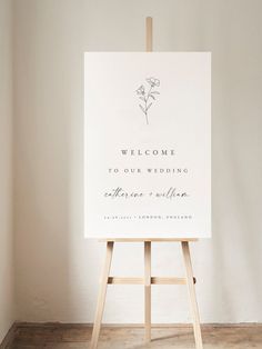 an easel with a welcome sign on it in front of a white wall and wooden floor