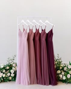 four bridesmaid dresses hanging on a rack in front of flowers