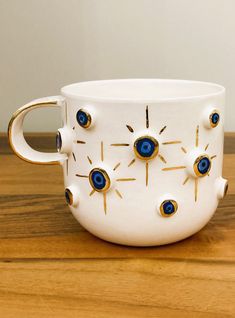 a white coffee cup with blue eyes and gold trimmings on it sitting on a wooden table