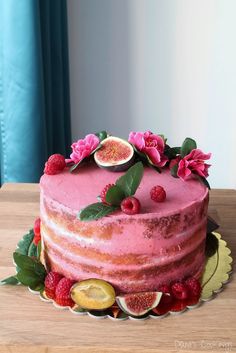 a pink cake with fresh fruit and flowers on top is sitting on a wooden table