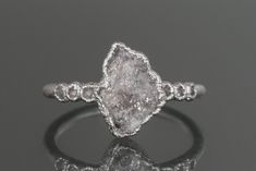 an engagement ring with a rough white diamond in the center, on a reflective surface