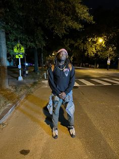 a man standing on the side of a road at night with his hands in his pockets