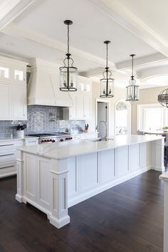 a large kitchen with white cabinets and an island that has lights hanging from the ceiling