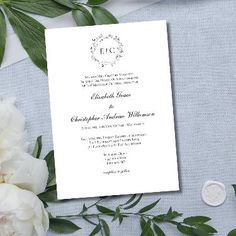 a white wedding card on top of a table with flowers and greenery around it