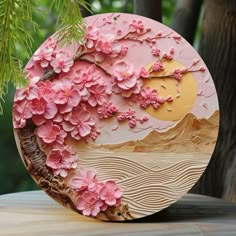 a wooden plate decorated with pink flowers on a table in front of trees and mountains