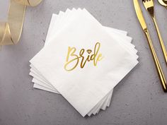 white napkins with gold foil lettering on them next to golden cutlery and ribbon