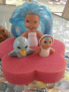 two dolls sitting on top of a pink heart shaped cake with an owl figurine next to it