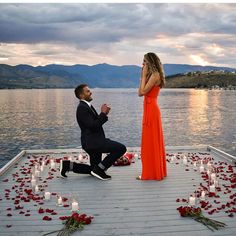 a man kneeling down next to a woman in an orange dress on a dock with candles