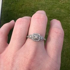 a person's hand with a diamond ring on top of their finger and grass in the background