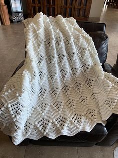 a white crocheted blanket sitting on top of a black leather chair in a living room