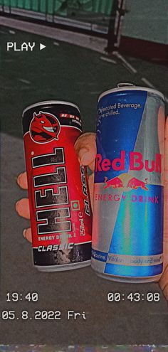 two cans of red bull energy drink are held up by someone's left hand