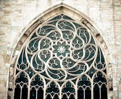 an ornate iron window on the side of a stone building with arched glass and wrought iron bars