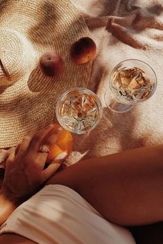 two people are toasting on the beach with fruit and drinks in their glasses next to them