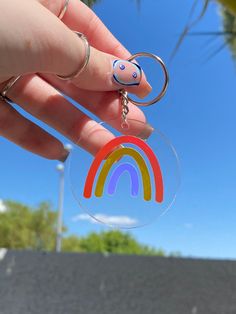 a hand holding a clear keychain with a rainbow painted on the front and side