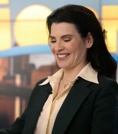 a smiling woman in a black jacket and white shirt is holding a cell phone with her right hand