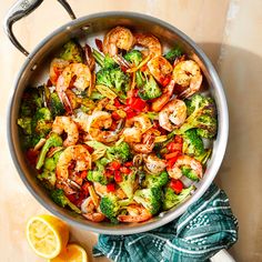 a pan filled with shrimp and broccoli next to lemon wedges on a table