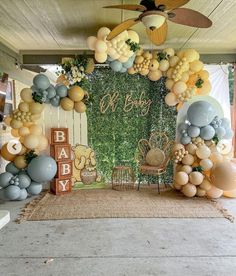 an outdoor baby shower with balloons and greenery on the wall, along with other decorations