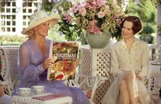 two women are sitting on a bench and one is reading a book while the other woman sits next to her