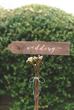 a wooden sign that says we do wedding with flowers in front of some green bushes